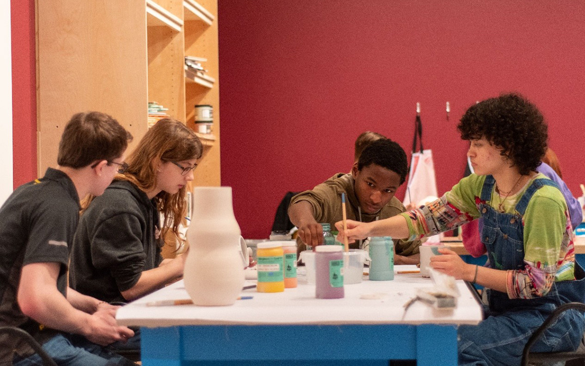 Four young adults sit at a table while painting pottery.