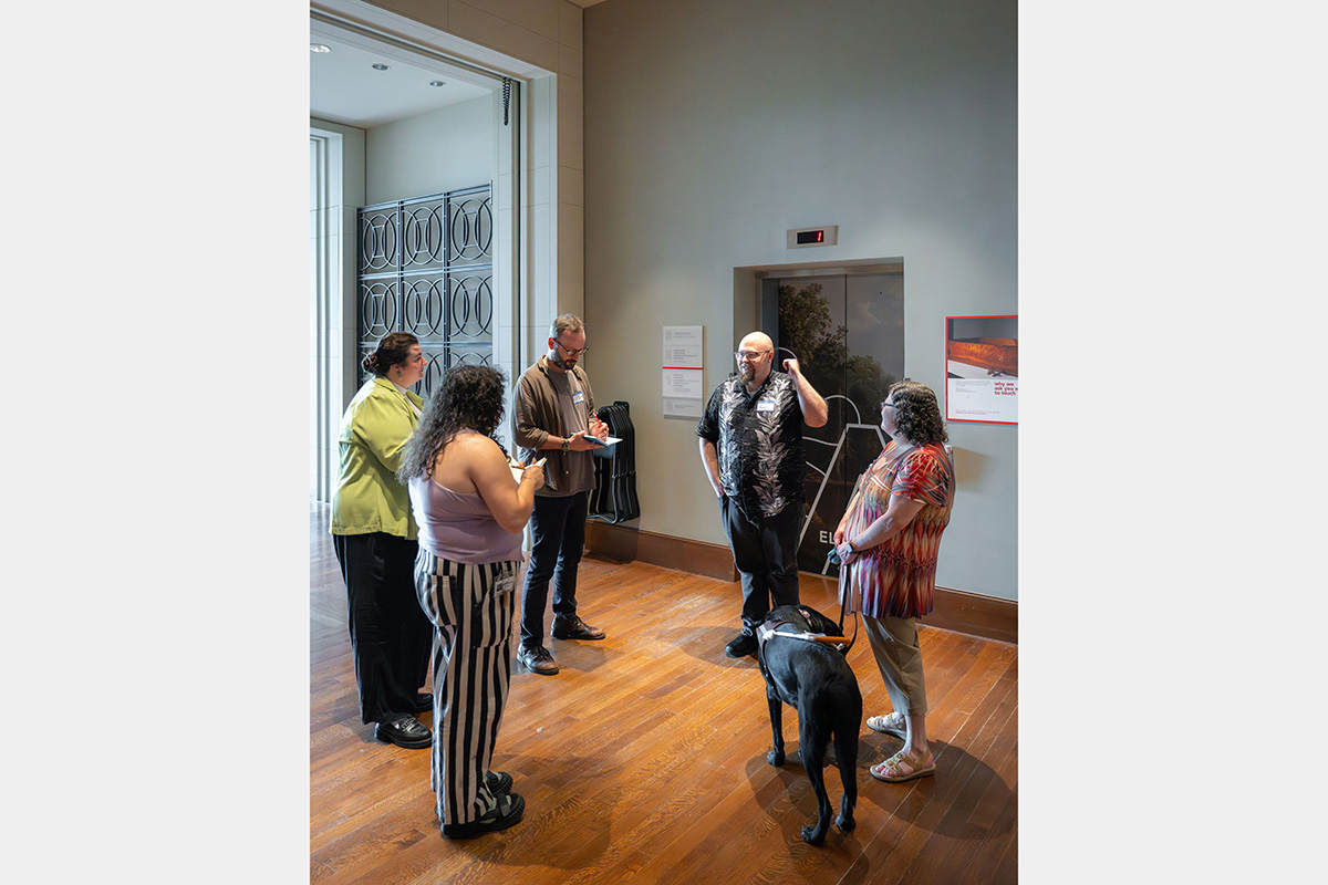 Five people and service dog standing next to an elevator.