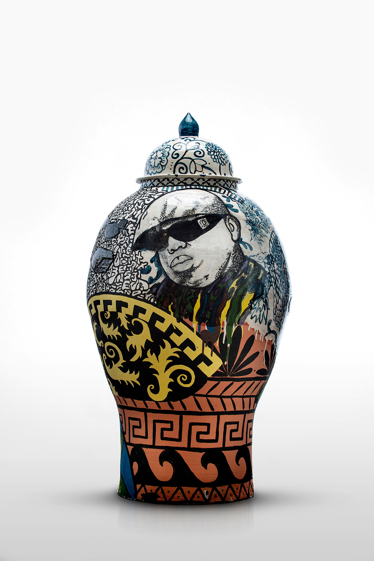 A white, blue, black, orange, and yellow glazed ceramic urn with many overlapping patterns. A man in a hat and sunglasses, the Notorious B.I.G. or Biggie, is featured.