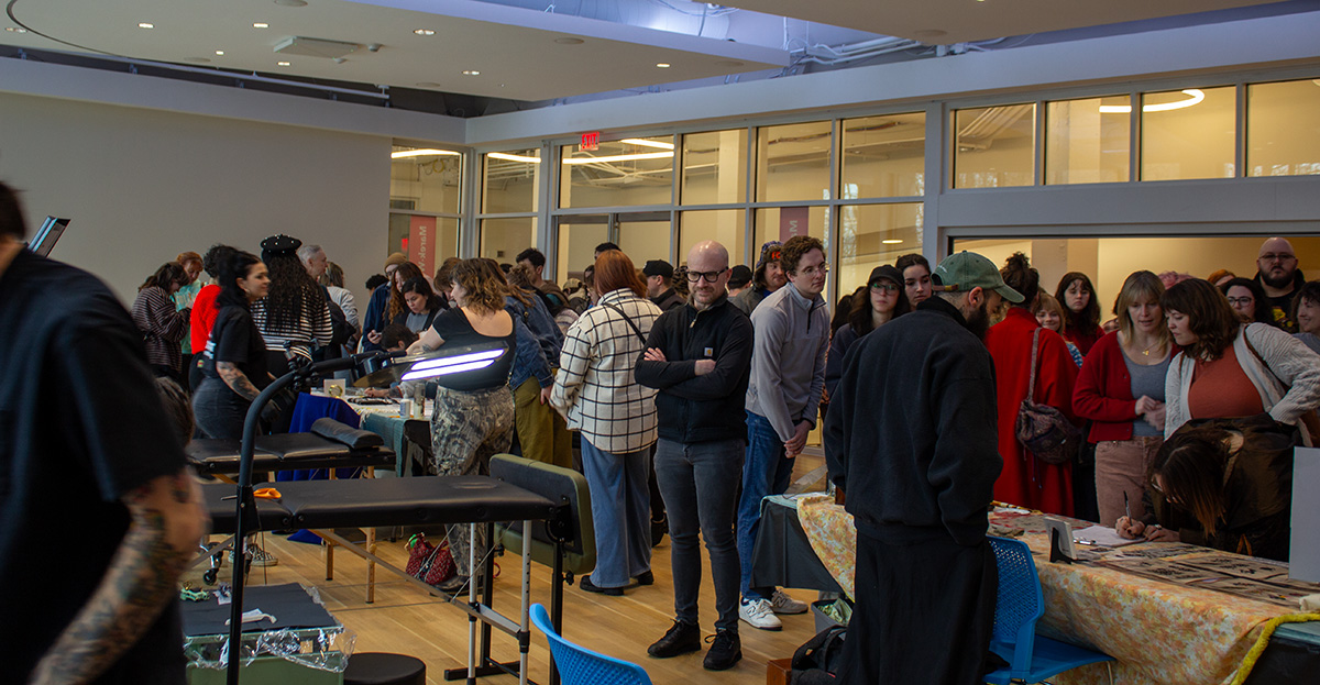 People crowd around tattoo artists displaying their designs