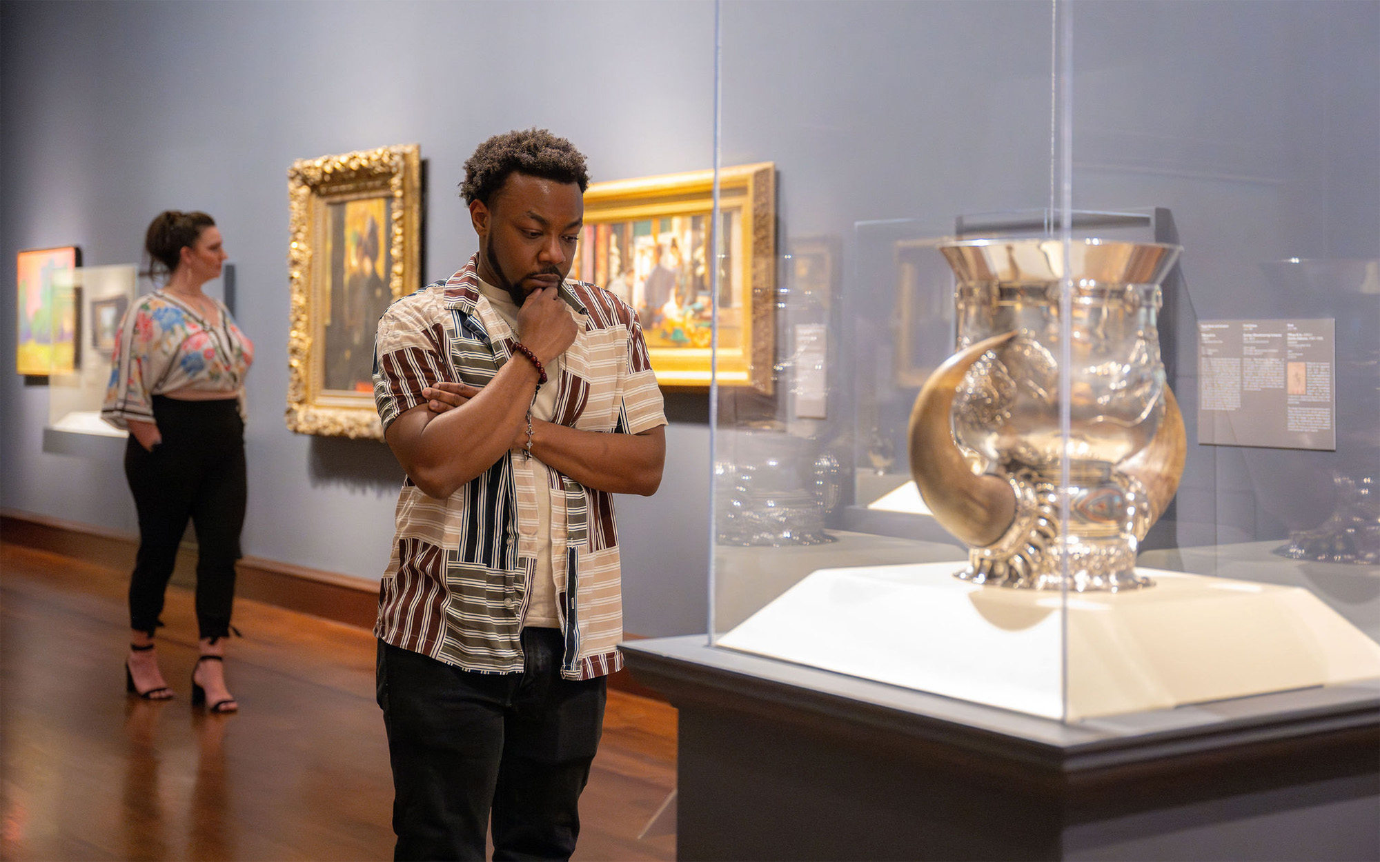 A Black man looks at a large silver pitcher in a glass case