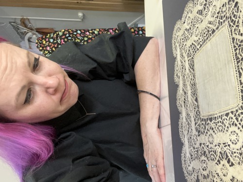 A white woman with purple hair looks at a piece of lace