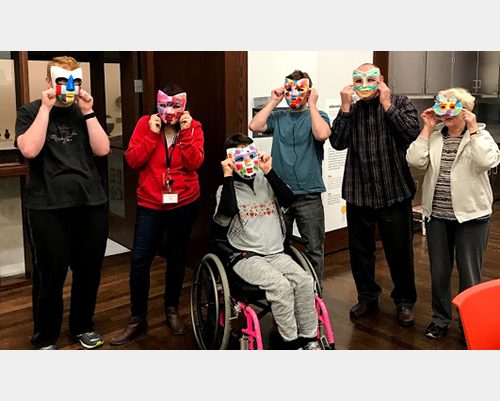 Participants hold handmade masks up to their faces for a photo