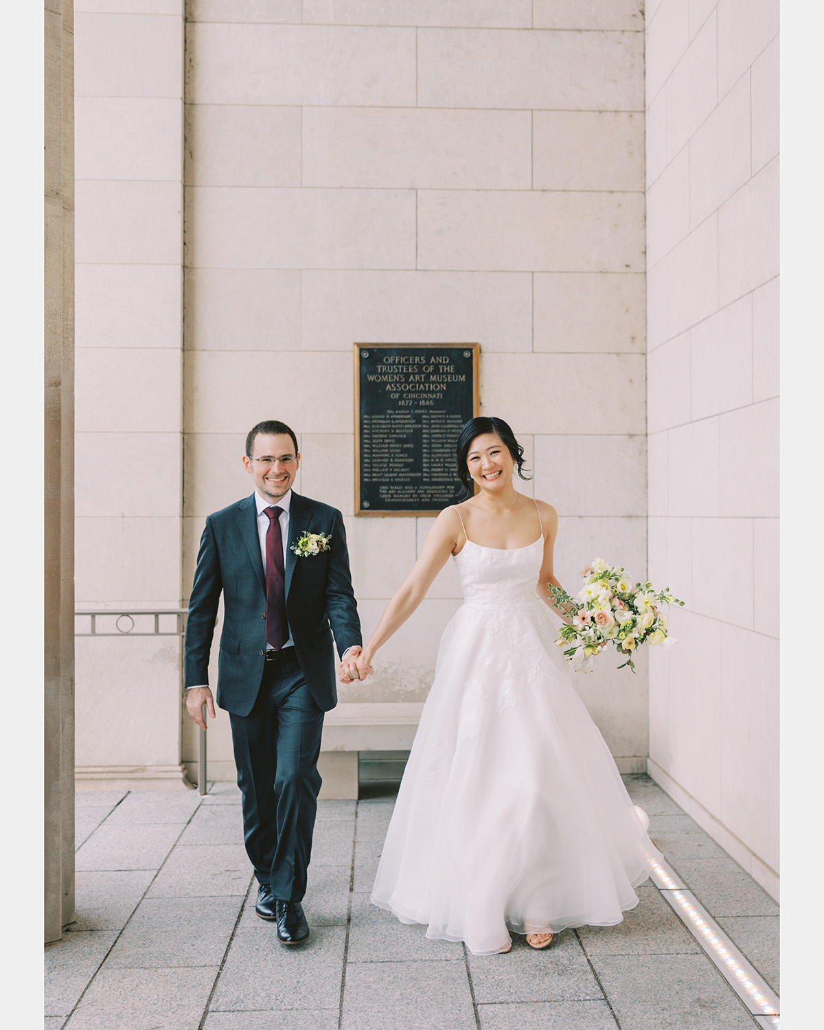 A smiling couple walks toward the photographer by the front entrance of the museum