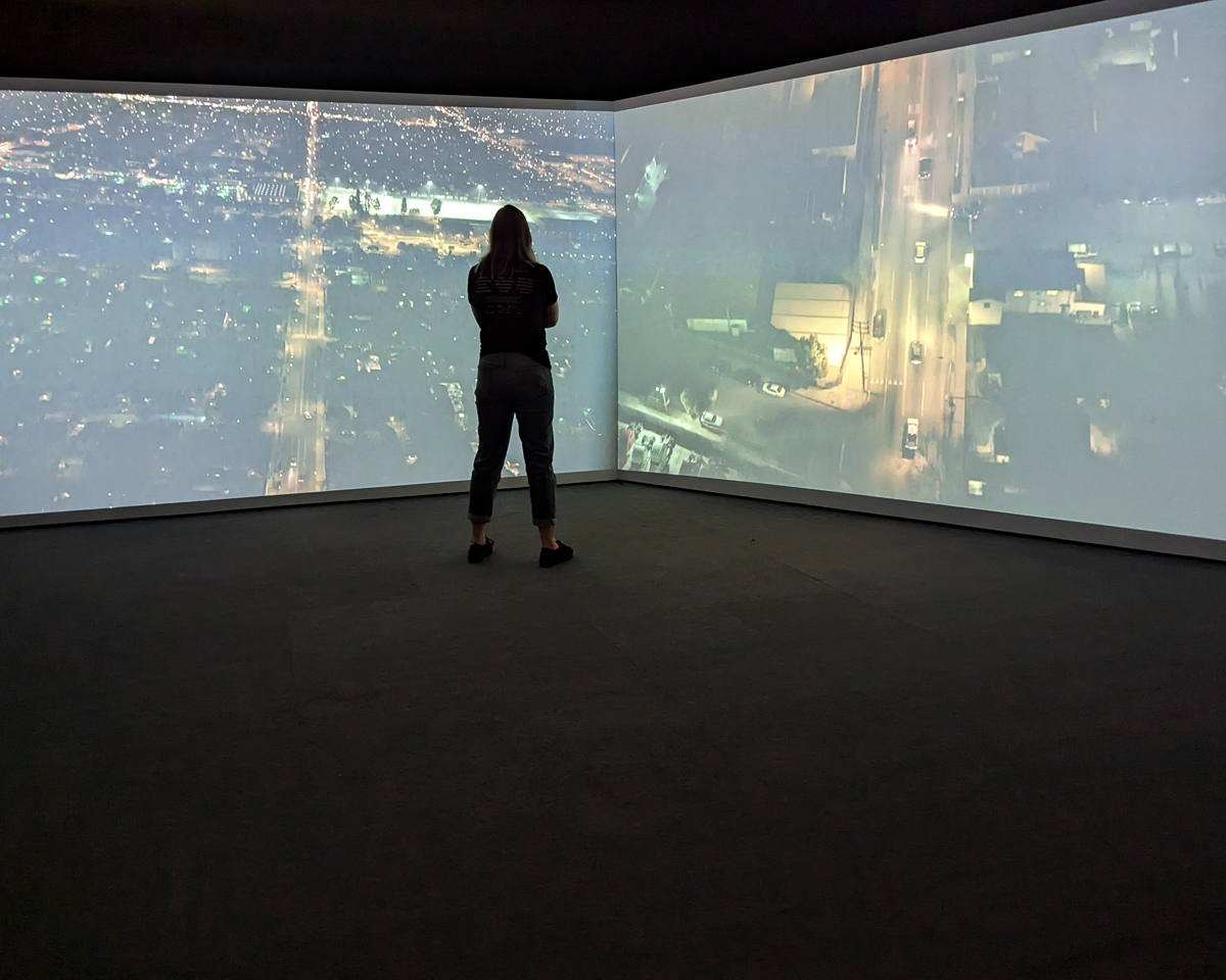 A visitor stands close to two large screens playing different videos of city streets