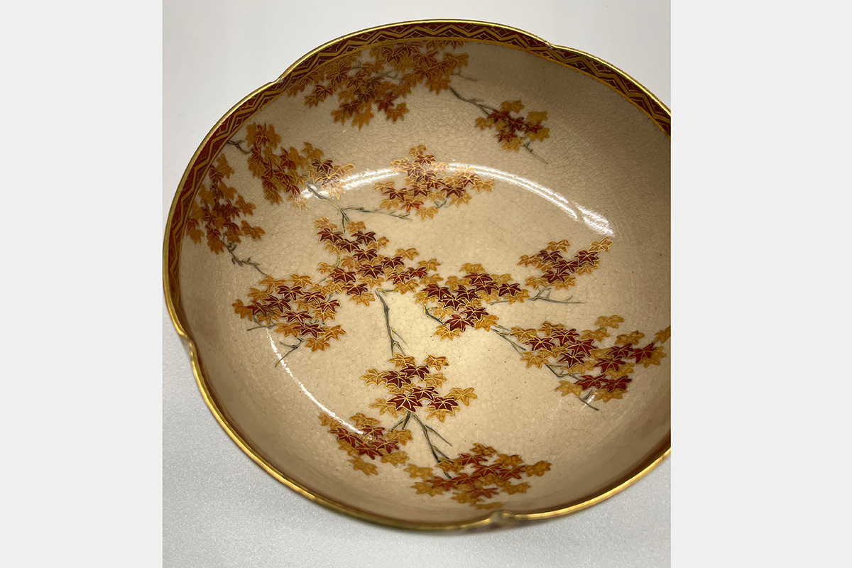 Interior of ceramic bowl featuring a painted design of dark tree branches and brightly colored leaves in hues of red and gold