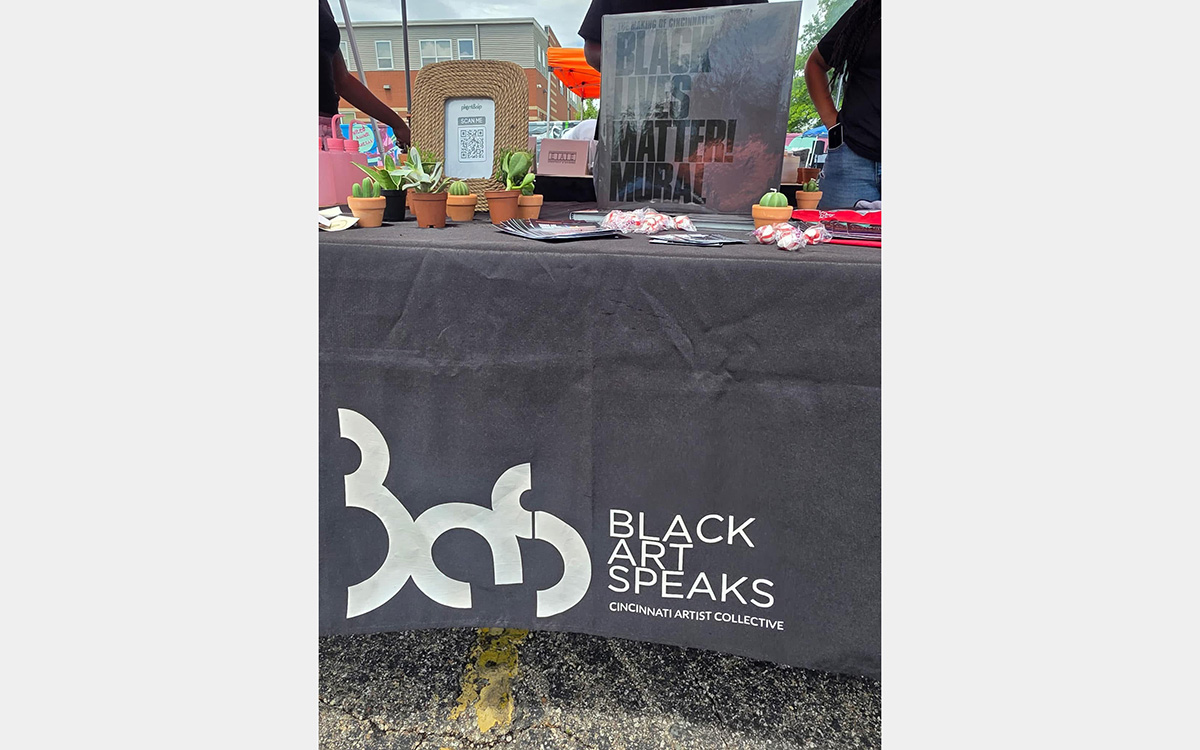 Dark gray table covering with "Black Art Speaks" over a table with plants and other items.