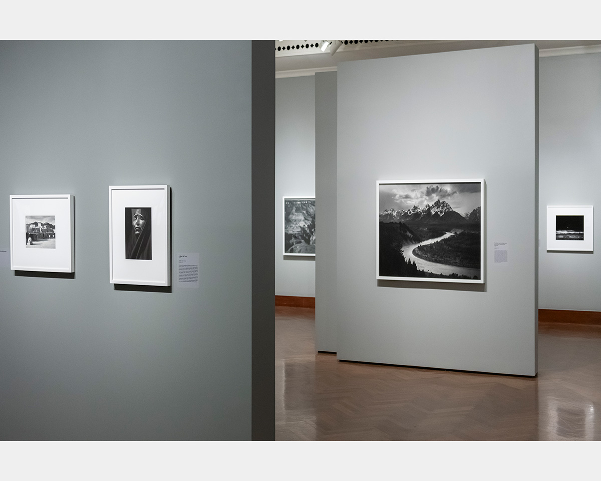 Framed black and white photographs hang on walls inside a gallery space.