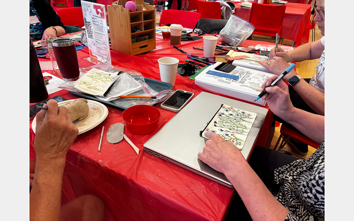 Photograph of hands making artwork on a red table top.