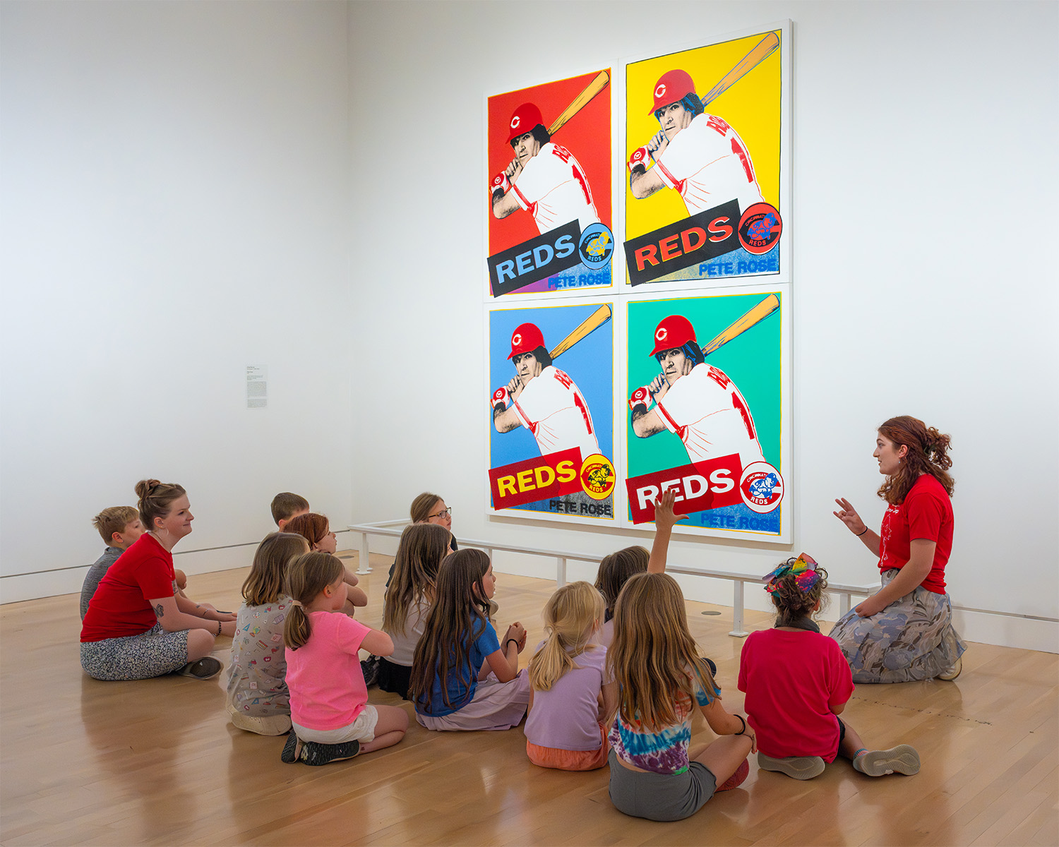 A group of students sit in front of a massive print and listen to a teacher