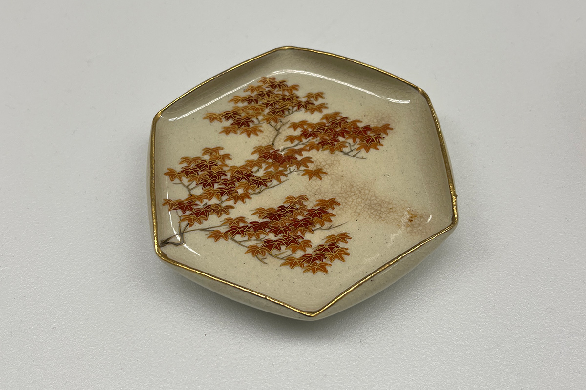 Ceramic dish featuring painted design of dark tree branches and brightly colored leaves in hues of red and gold