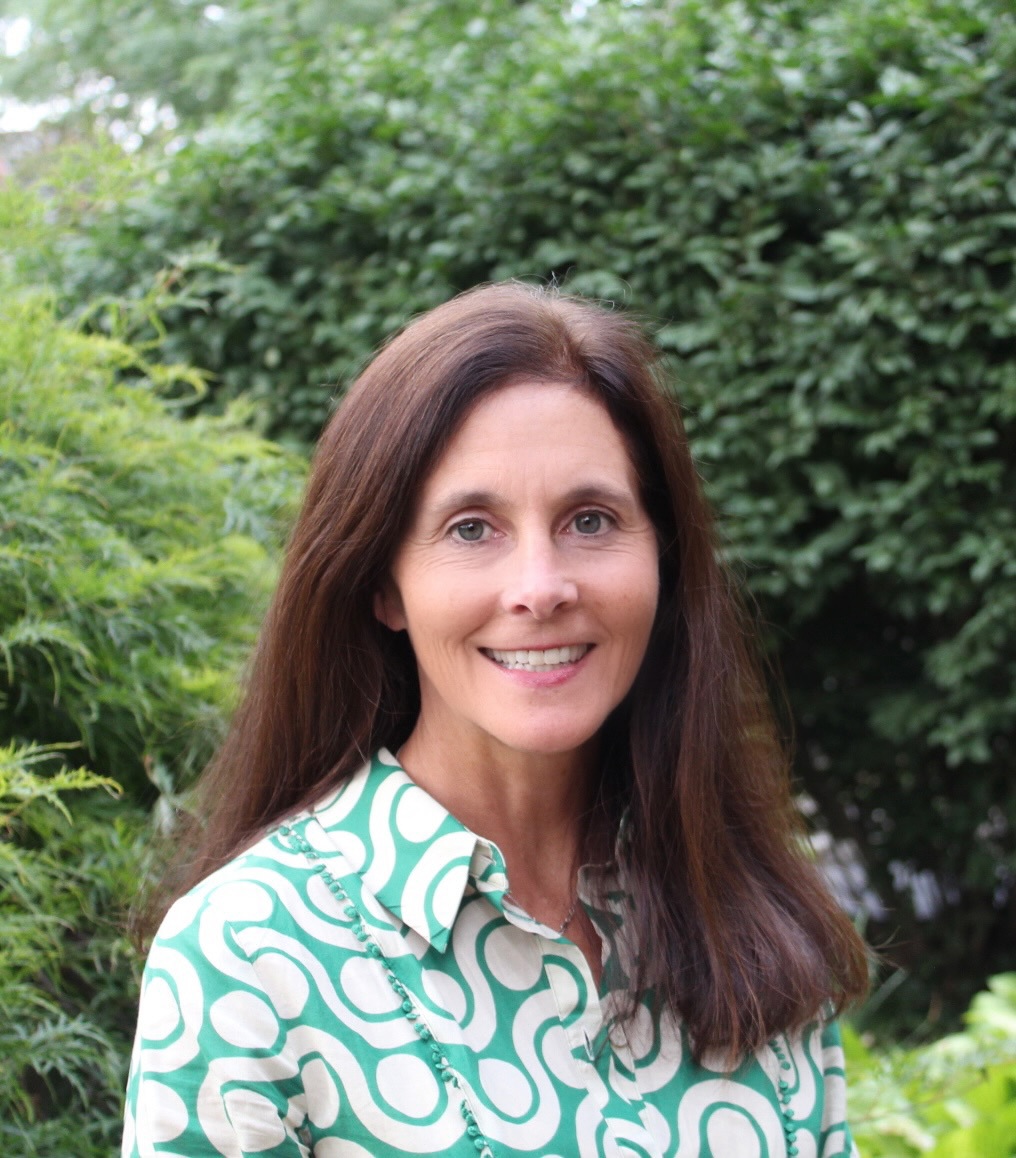 A smiling white woman with brown hair wearing a swirly green and white top.