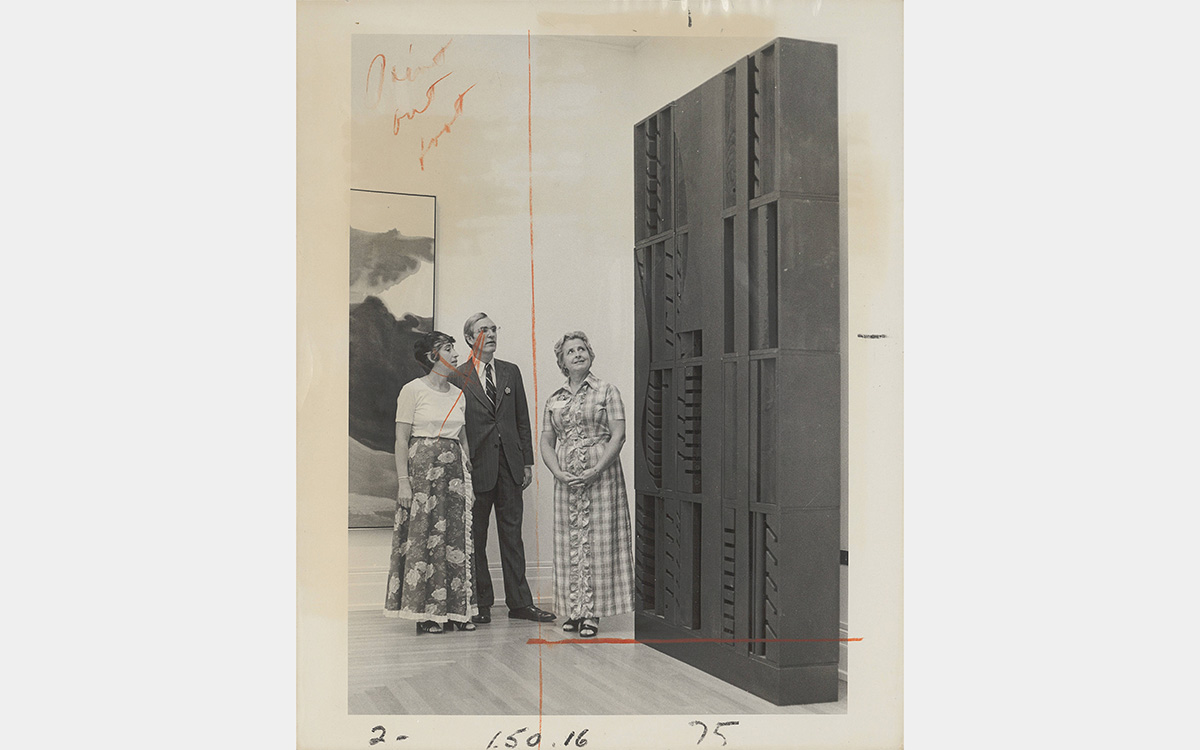 Black and white photo of three people looking at a box-like sculpture