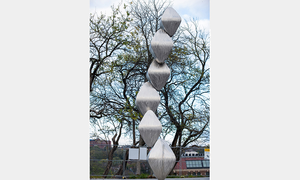 A tall statue of brushed metal diamonds stacked atop each other in a spiral pattern