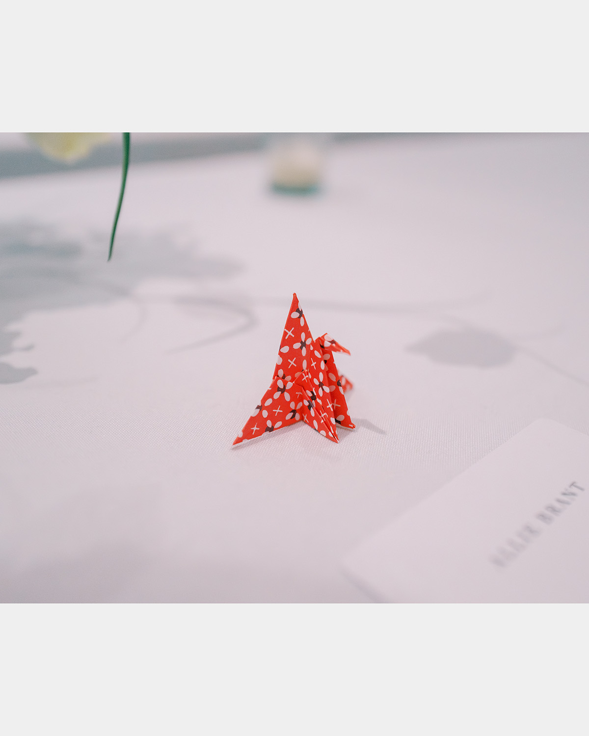 A small origami paper crane on bright red paper with a floral design