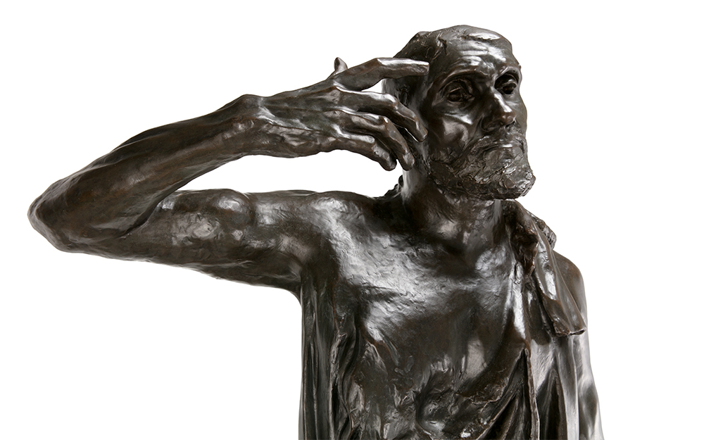 A rough, dark sculpture of a man wearing a robe with their hand reaching towards their face.