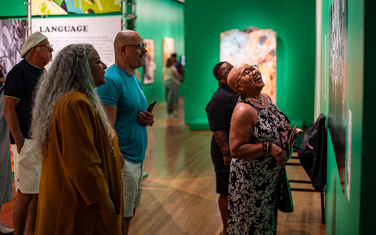 A Black woman laughs as she looks closely at an artwork on a green wall