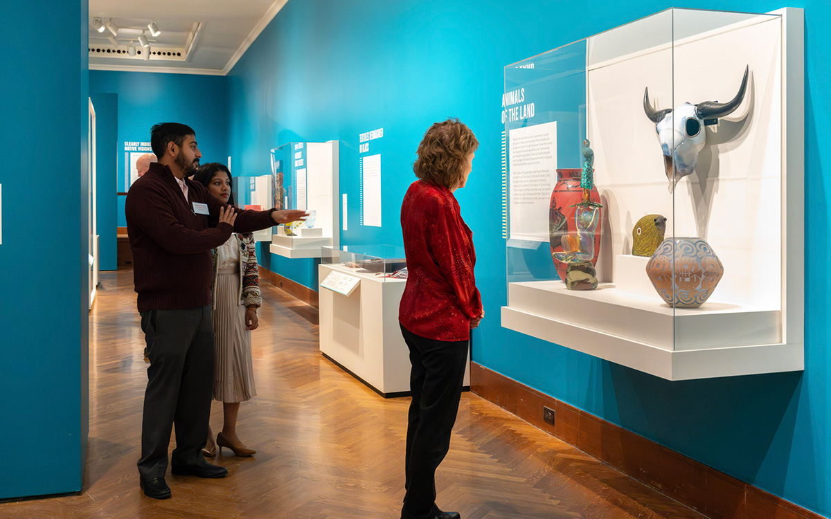 Three visitors admire a case full of glass art in a gallery