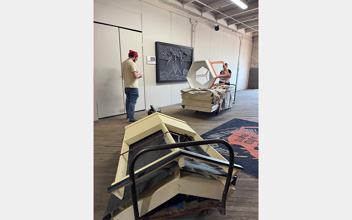 Two people with carts filled with large wood parts inside a large room.