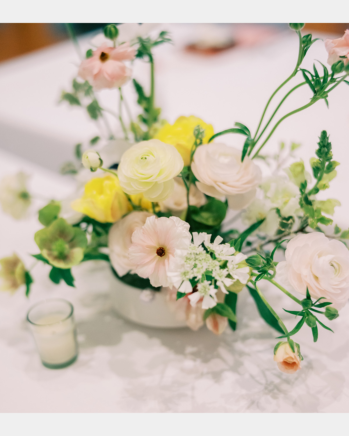 A floral arrangement on a table with light pink, yellow and white flowers